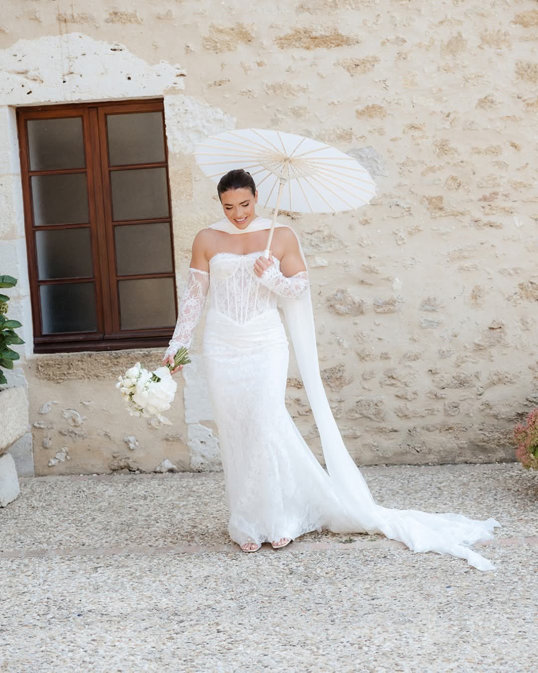 Bride in a long veil beside a stone wall at the château