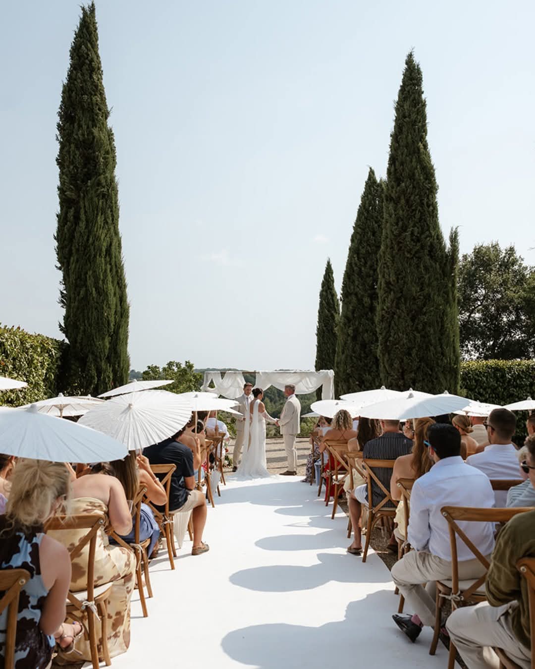 Wedding ceremony aisle between rows of guests under white parasols