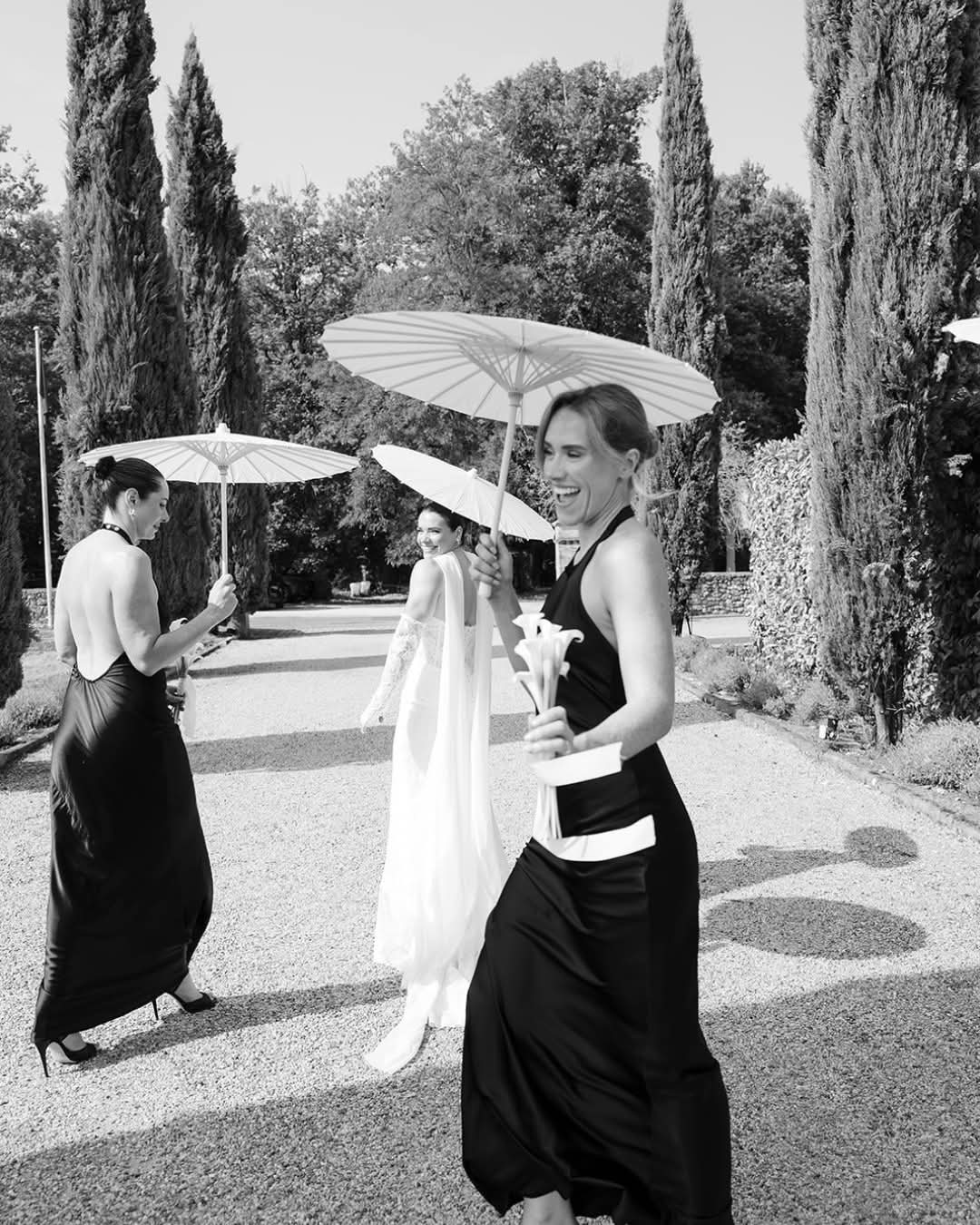 Bride and bridesmaid walking beneath parasols, in black and white