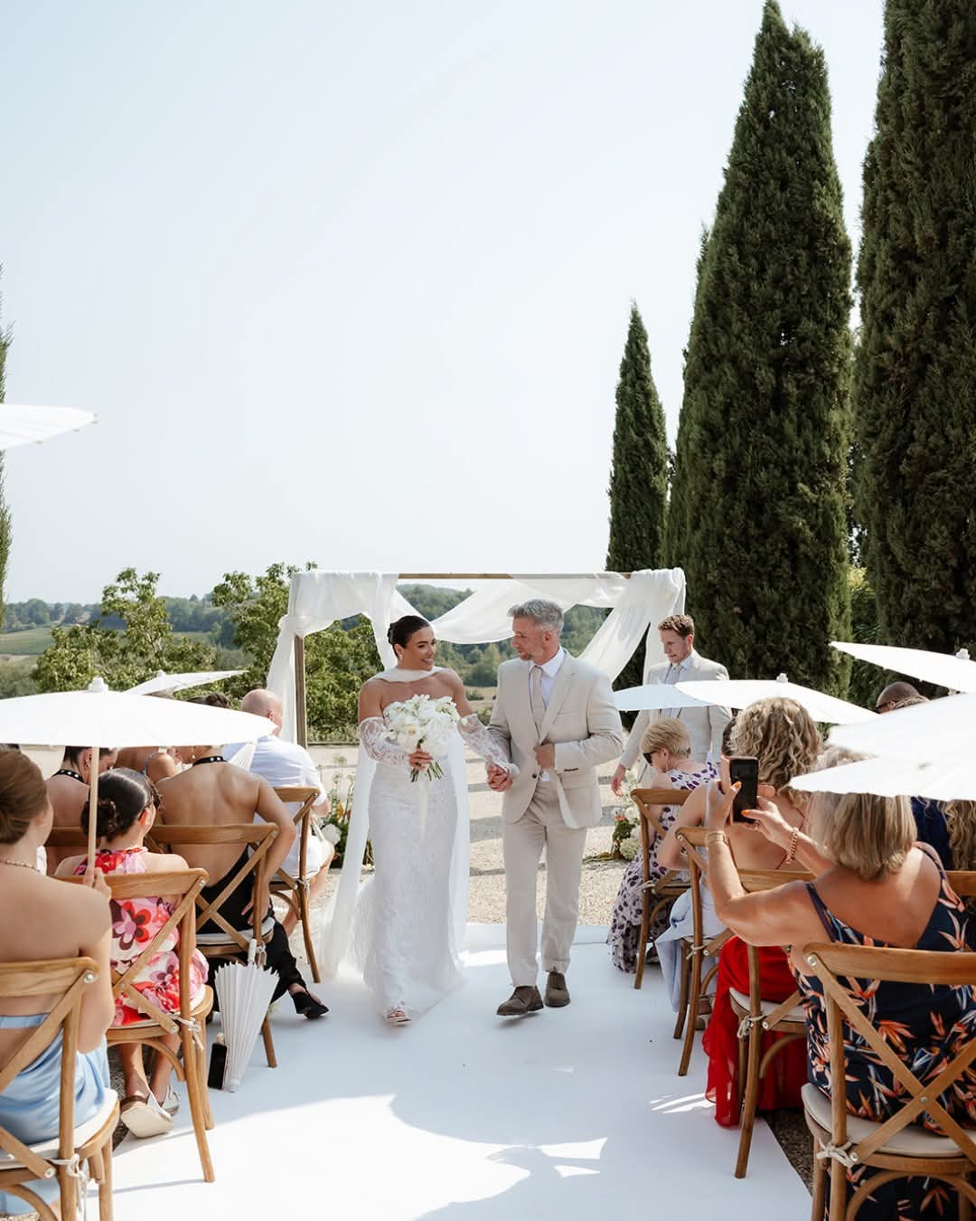 Bride walking down the aisle between cypress trees