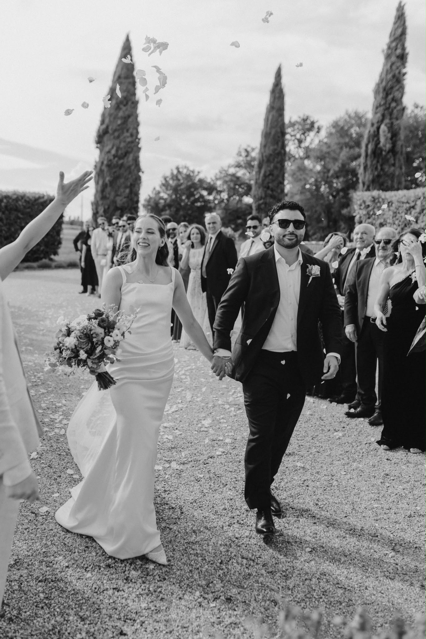 Newlyweds walking through cheering guests, in black and white