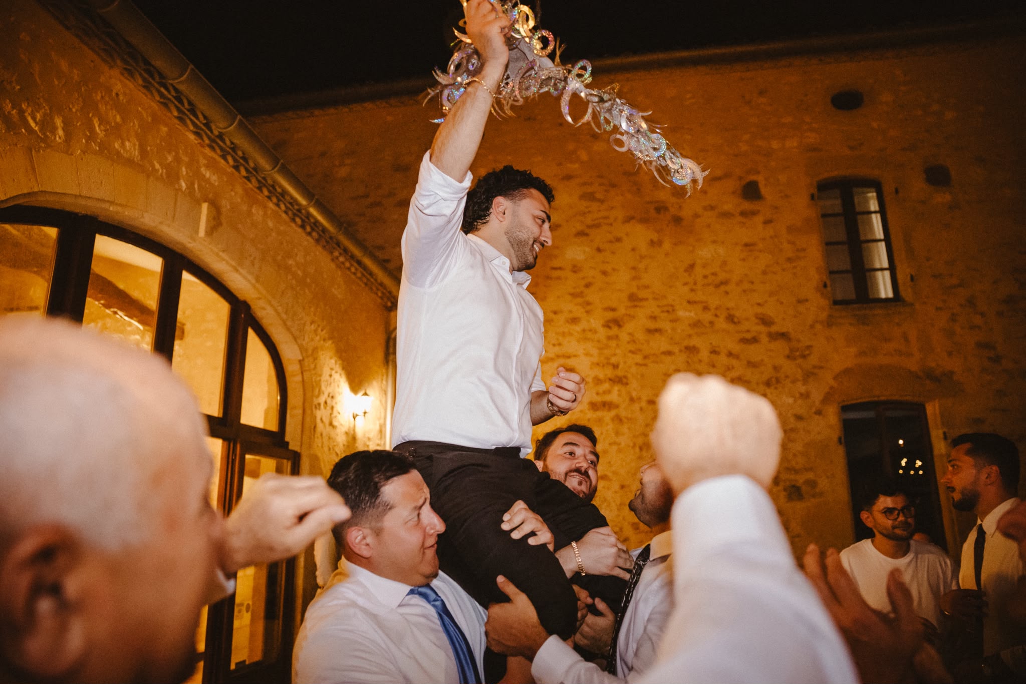 Groom held aloft by guests inside the stone barn